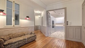 A hallway with a patterned sofa, a radiator, and a kitchen area with white cabinets. - RIGHT AROUND THE CORNER, NEAR EVERYWHERE YOU WANT TO BE–SAINT GERMAIN (Paris)