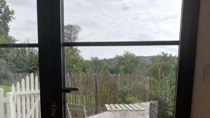A view through a glass door into a backyard with a white fence, a stone patio, and a wooden deck.