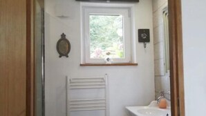 A small, well-lit bathroom with a window, a radiator, a sink, and a mirror.