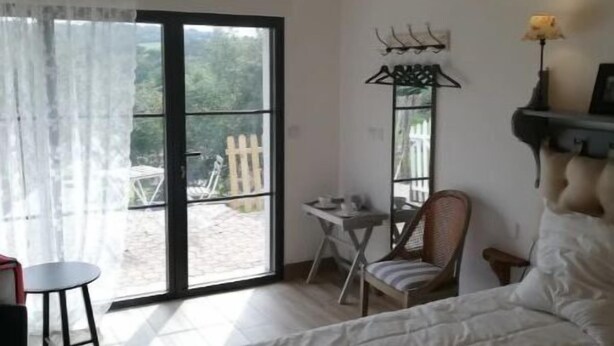 A bedroom with a bed, a desk, a chair, a hanging light fixture, and a view through a glass door.