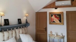 A bedroom with a large bed, a chandelier, a wooden wardrobe, and a small table with decorative items.
