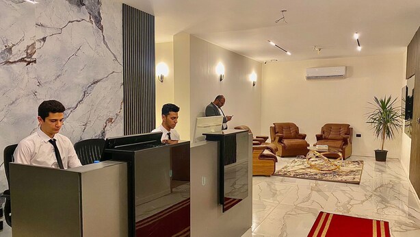 A hotel reception area with marble walls, a reception desk, and seating with a red carpet. - Golden House  (New Cairo)