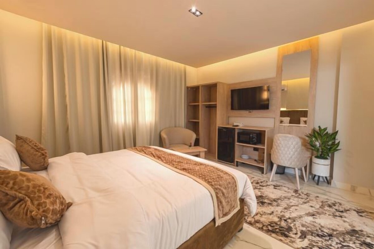 A modern bedroom with a large bed, a TV, a desk, and a chair.