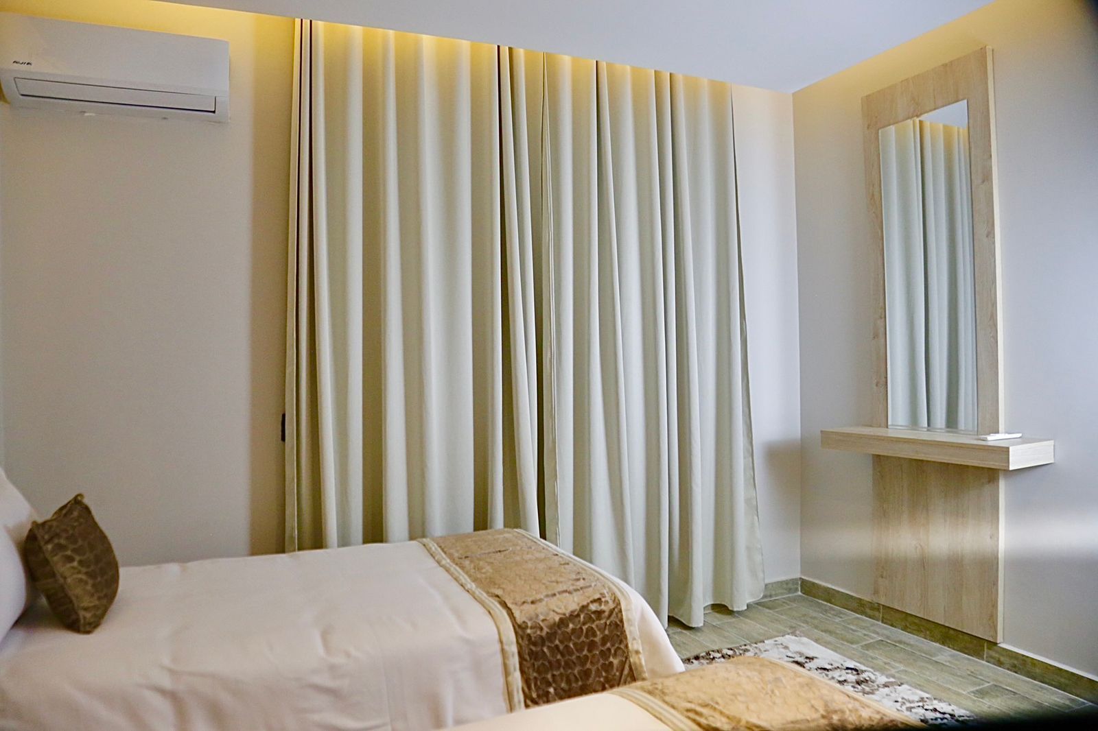 A hotel room with a bed, a bedside table, a mirror, and a window with curtains.