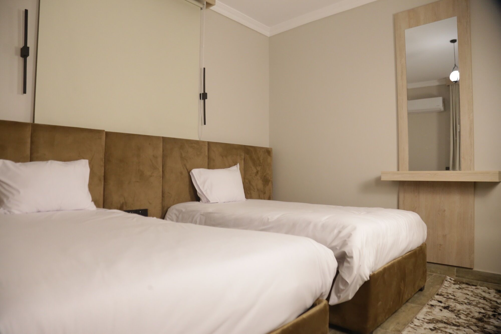 A hotel room with two beds, a wooden headboard, a mirror, and a light fixture.