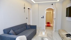 A modern living room with a grey sofa, a white armchair, a small wooden coffee table, and a TV mounted on the wall. - Golden House  (New Cairo)