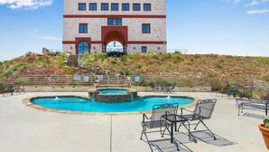 A pool area with a large building in the background, a hot tub, and outdoor seating.