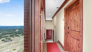 A hallway with a red carpet, wooden doors, and a view of a landscape.