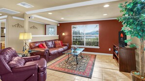 A living room with a brown leather sofa, a glass coffee table, and a large window with blinds. - Experience ranch living at Lighthouse Hill Ranch - Red House on 2001 acres! (Johnson City)