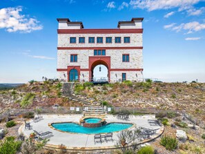 Un grande edificio a più piani con un'imponente entrata ad arco, una piscina e un'area salotto all'aperto.