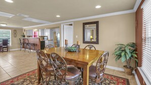 A dining area with a wooden table and chairs, a kitchen in the background, and a potted plant. - Experience ranch living at Lighthouse Hill Ranch - Red House on 2001 acres! (Johnson City)