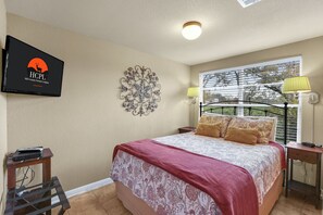 Una camera da letto con un letto, una TV fissata al muro, un elemento decorativo a parete e una finestra vista alberi.
