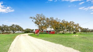A rural road leading to a red barn and a white building, surrounded by trees and open fields. - Experience ranch living at Lighthouse Hill Ranch - Red House on 2001 acres! (Johnson City)