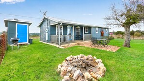 A two-story house with a porch, a blue door, and a stone fire pit in the yard. - Hilltop Ranch Stay on 2,001 Acres | Shared Pool, Hot Tub & Trails (Johnson City)