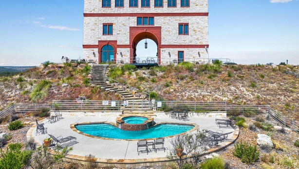 A large, multi-story building with a prominent arched entrance, a swimming pool, and outdoor seating. - Hilltop Ranch Stay on 2,001 Acres | Shared Pool, Hot Tub & Trails (Johnson City)