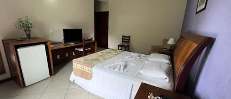Une chambre d’hôtel équipée d’un lit, d’un bureau avec un ordinateur, d’un réfrigérateur et d’une télévision.