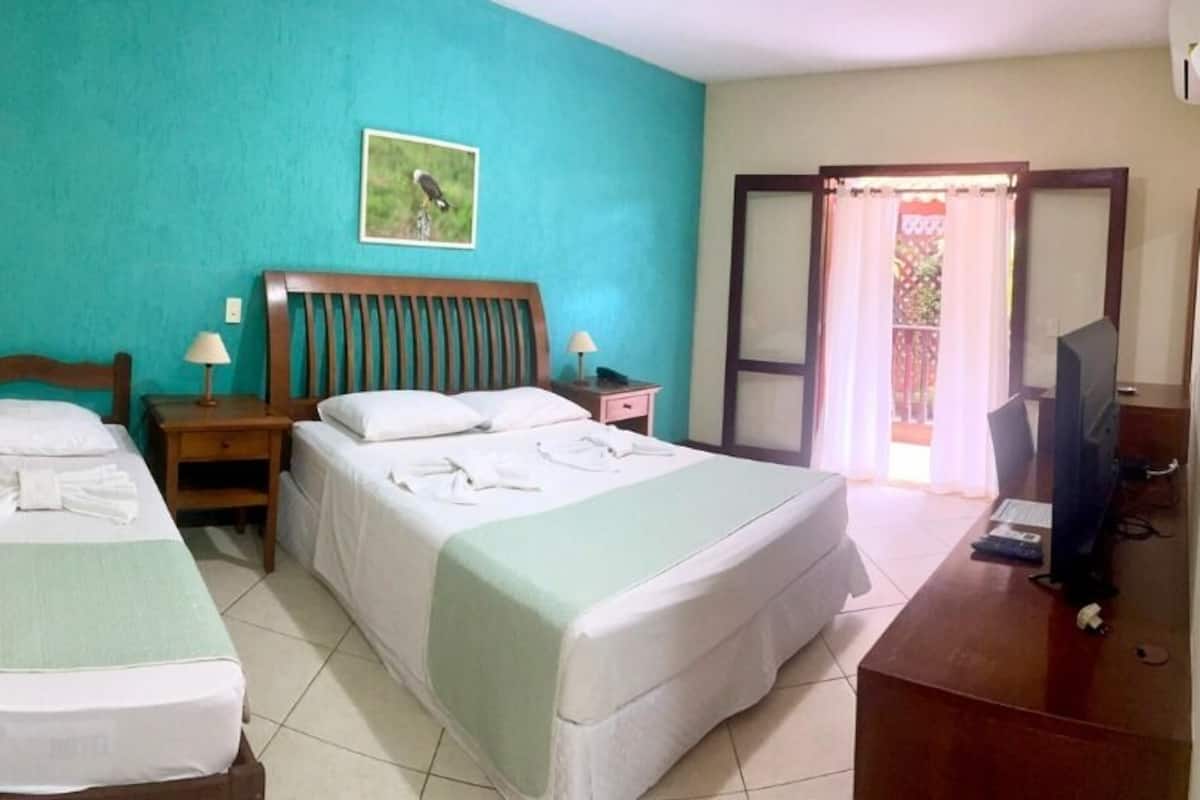 A hotel room with two single beds, a wooden headboard, a desk with a computer, and a balcony with a view.