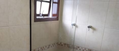 A small, enclosed shower area with a glass door, a toilet, and a window above the toilet.