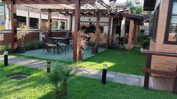 Área de pátio com mobiliário externo, pérgola e um edifício de tijolos com placas.