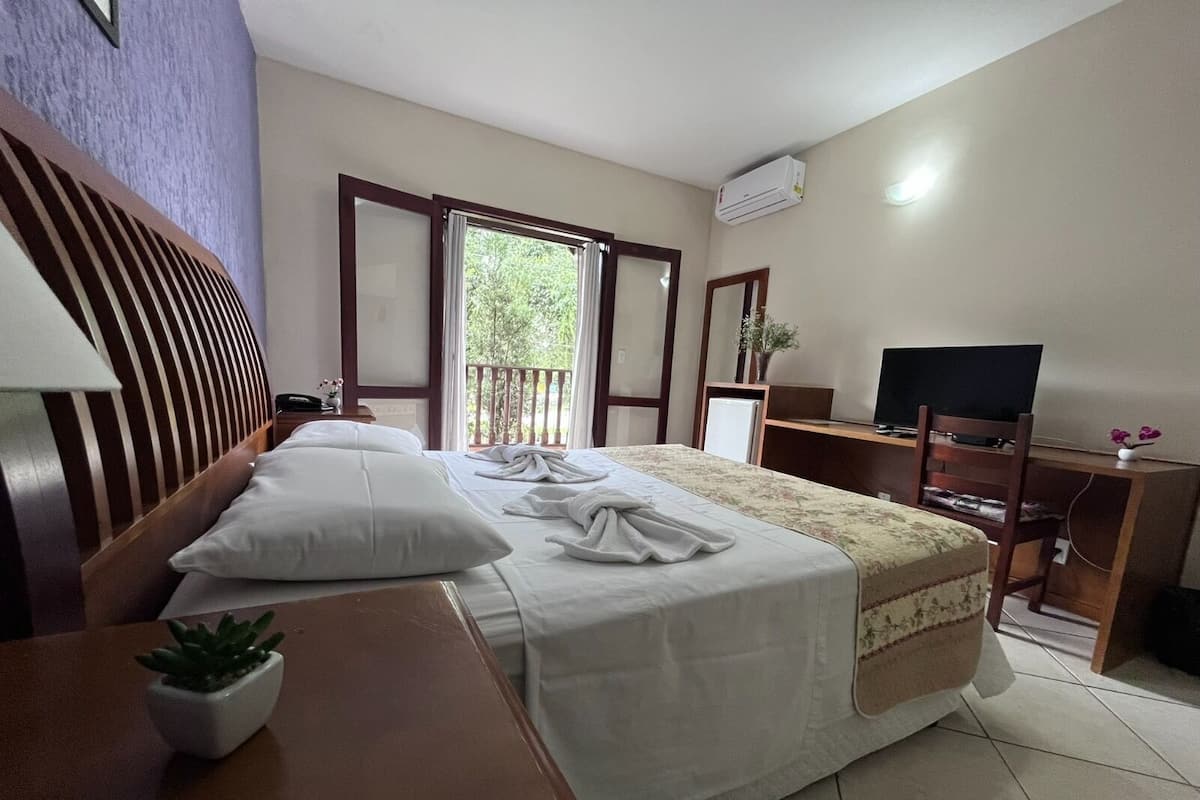 A hotel room with a bed, a desk, a TV, and an air conditioning unit.