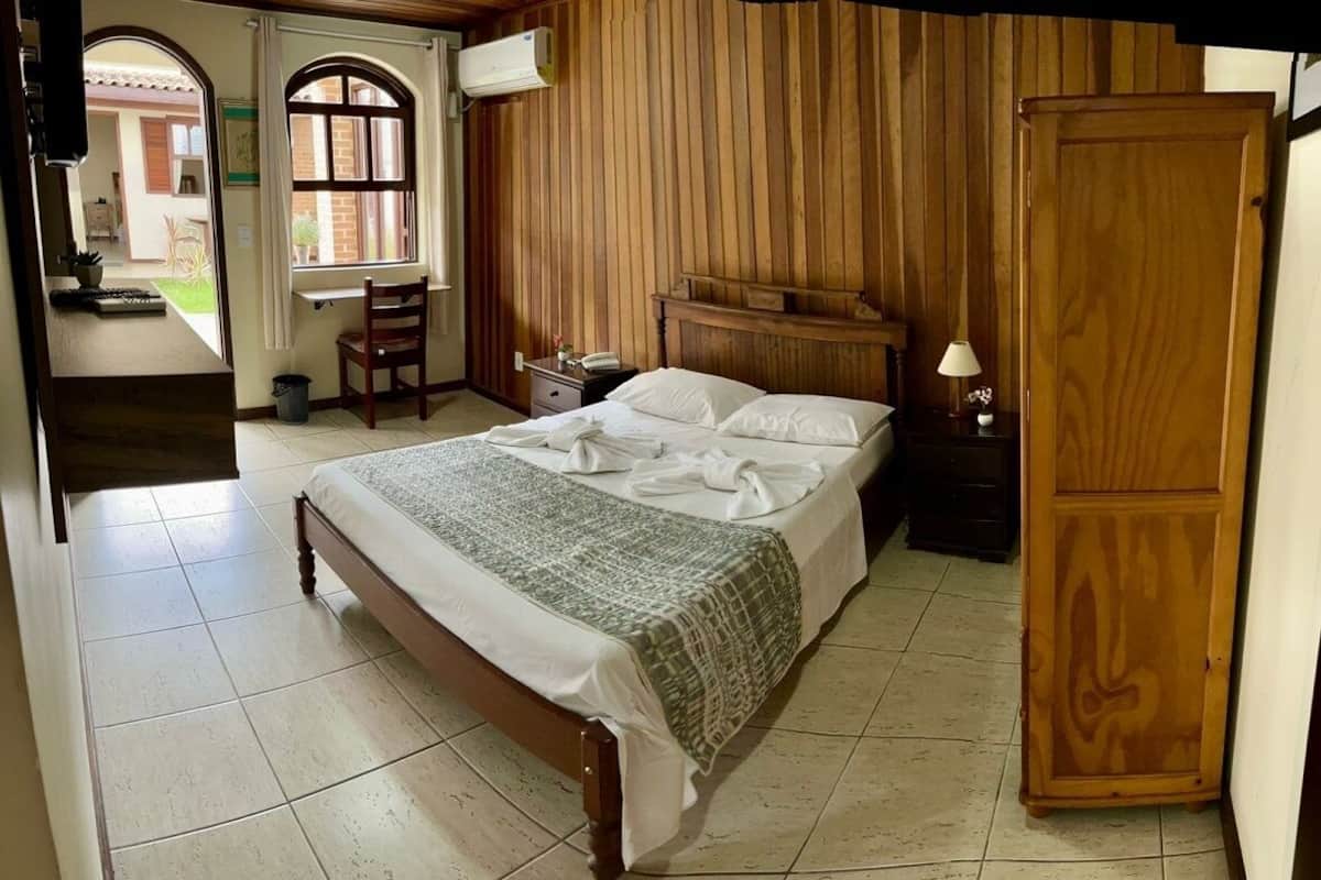 A bedroom with a wooden bed, a nightstand, a wooden wardrobe, and a window with curtains.