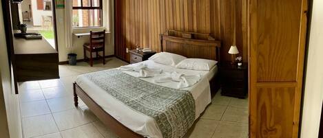 A bedroom with a wooden bed, a nightstand, a wooden wardrobe, and a window with curtains.