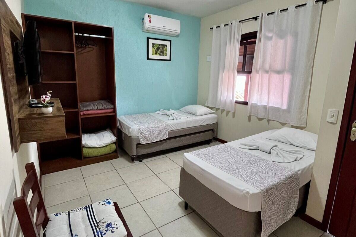 A compact room with two beds, a chair, a wardrobe, and an air conditioning unit.