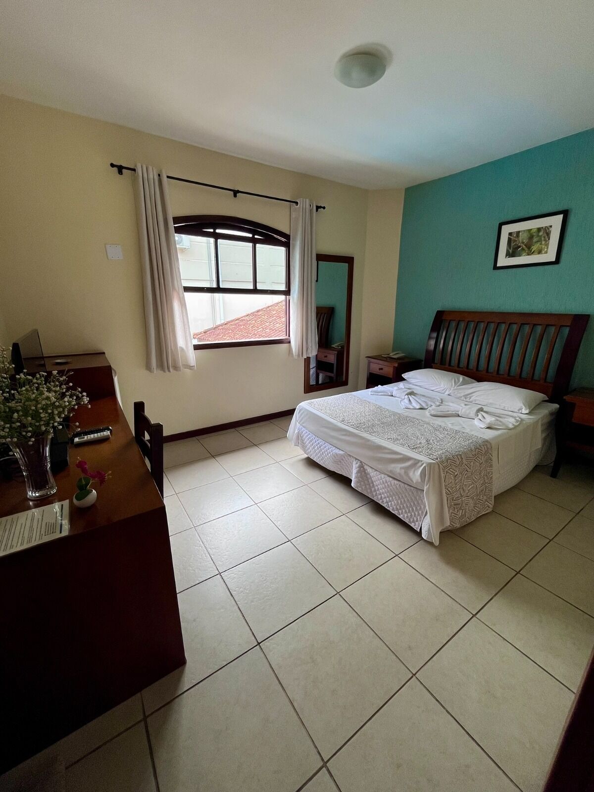A bedroom with a bed, a desk, a chair, a window with curtains, and a picture on the wall.