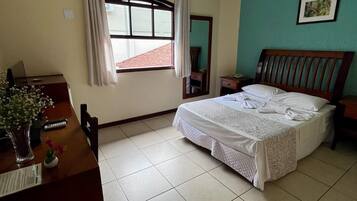 A bedroom with a bed, a desk, a chair, a window with curtains, and a picture on the wall.