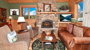 A cozy living room with a stone fireplace, wooden furniture, and a view of the outdoors. - Lakeside Chalet - Luxury Retreat on Grand Lake w/ Dock & Kayaks (Grand Lake)