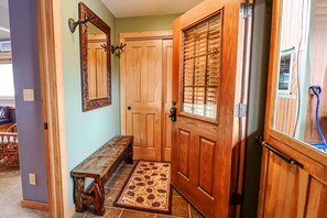 A wooden front door with a glass panel, a bench, a door mat, and a wall-mounted mirror.