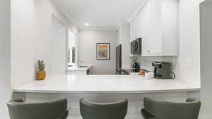 A modern kitchen with white cabinetry, a central island with seating, a coffee machine, and a pineapple on the counter. - Views and location, great villa in Turtle Point (Kiawah Island)