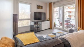 Habitación de hotel moderna con una cama grande, televisión, escritorio y balcón con mobiliario exterior.