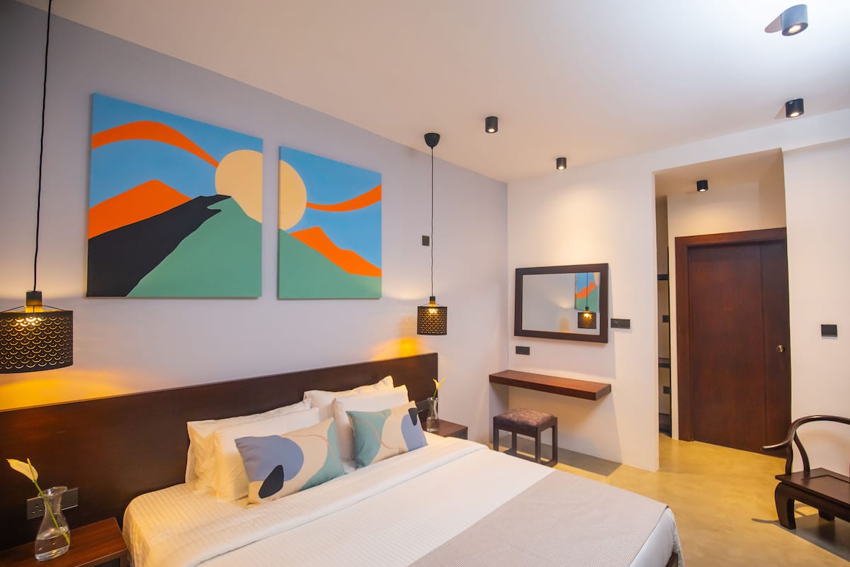 A modern hotel room with a large bed, two wall art pieces, a desk with a chair, and a door.