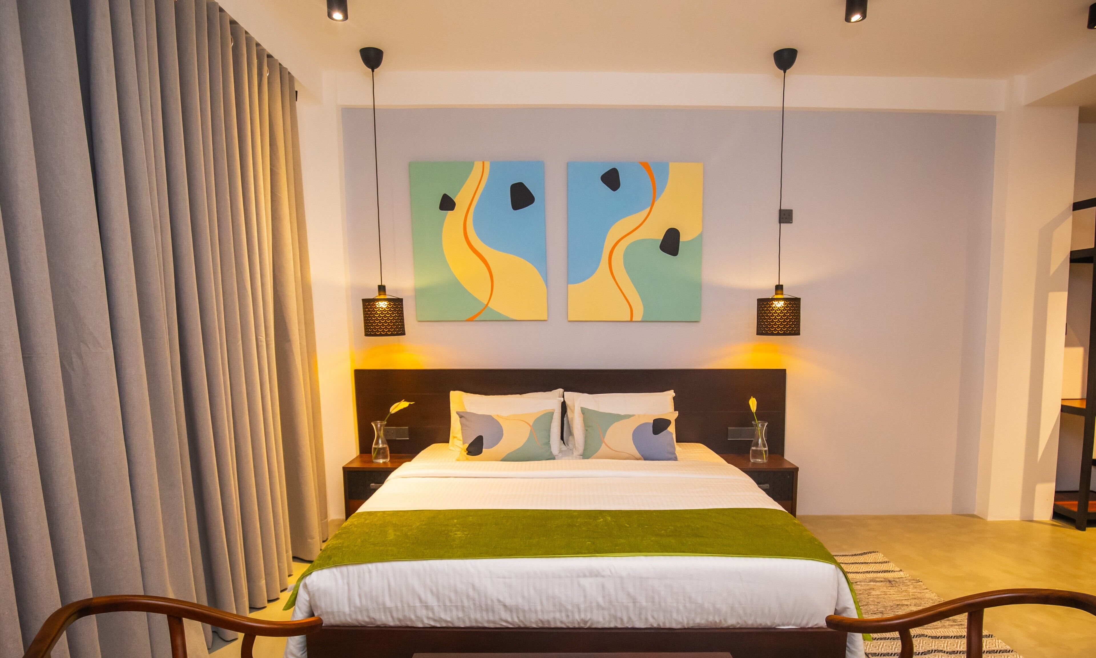 A modern bedroom with a large bed, two side tables, abstract wall art, and a patterned rug.