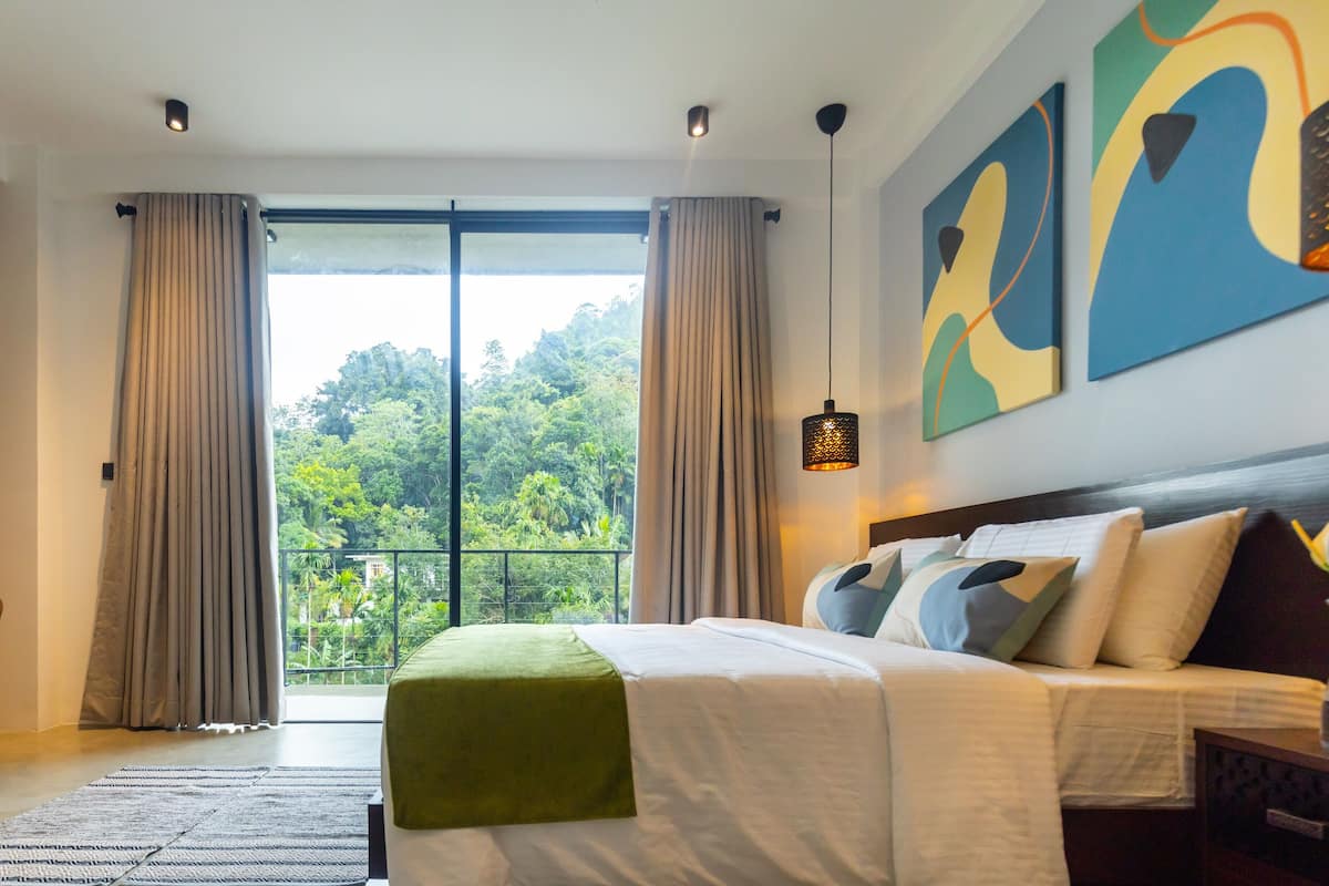 A bedroom with a bed, curtains, a view of greenery, and abstract art on the wall.