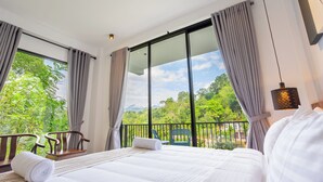 Habitación de hotel con una cama grande, vistas a zonas verdes y un balcón con sillas.