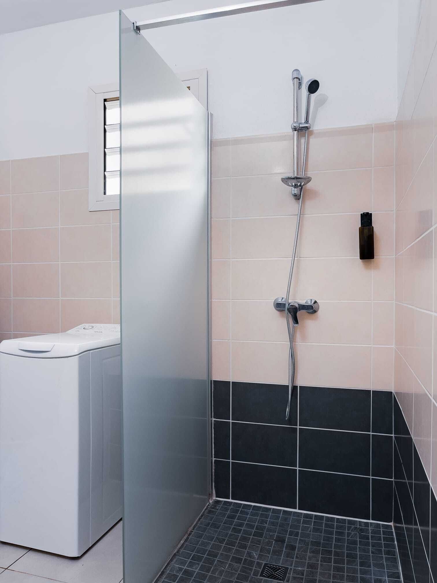 Une salle de bain moderne avec une douche à l’italienne en verre, des toilettes et un sol carrelé de couleur noire.