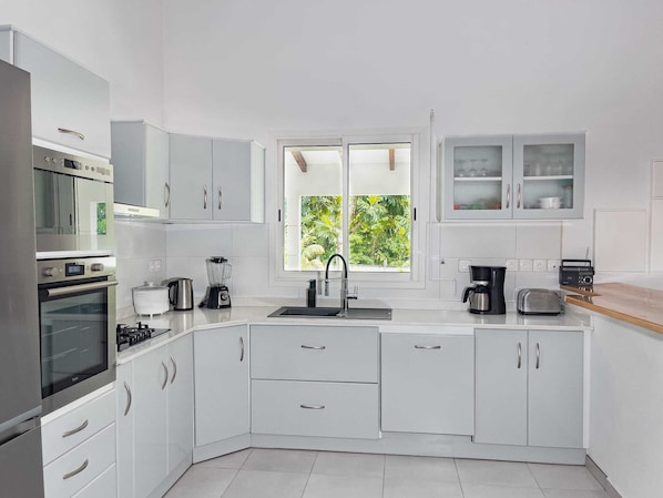 A modern kitchen with white cabinets, a built-in oven, a coffee maker, and a window with a view of greenery.