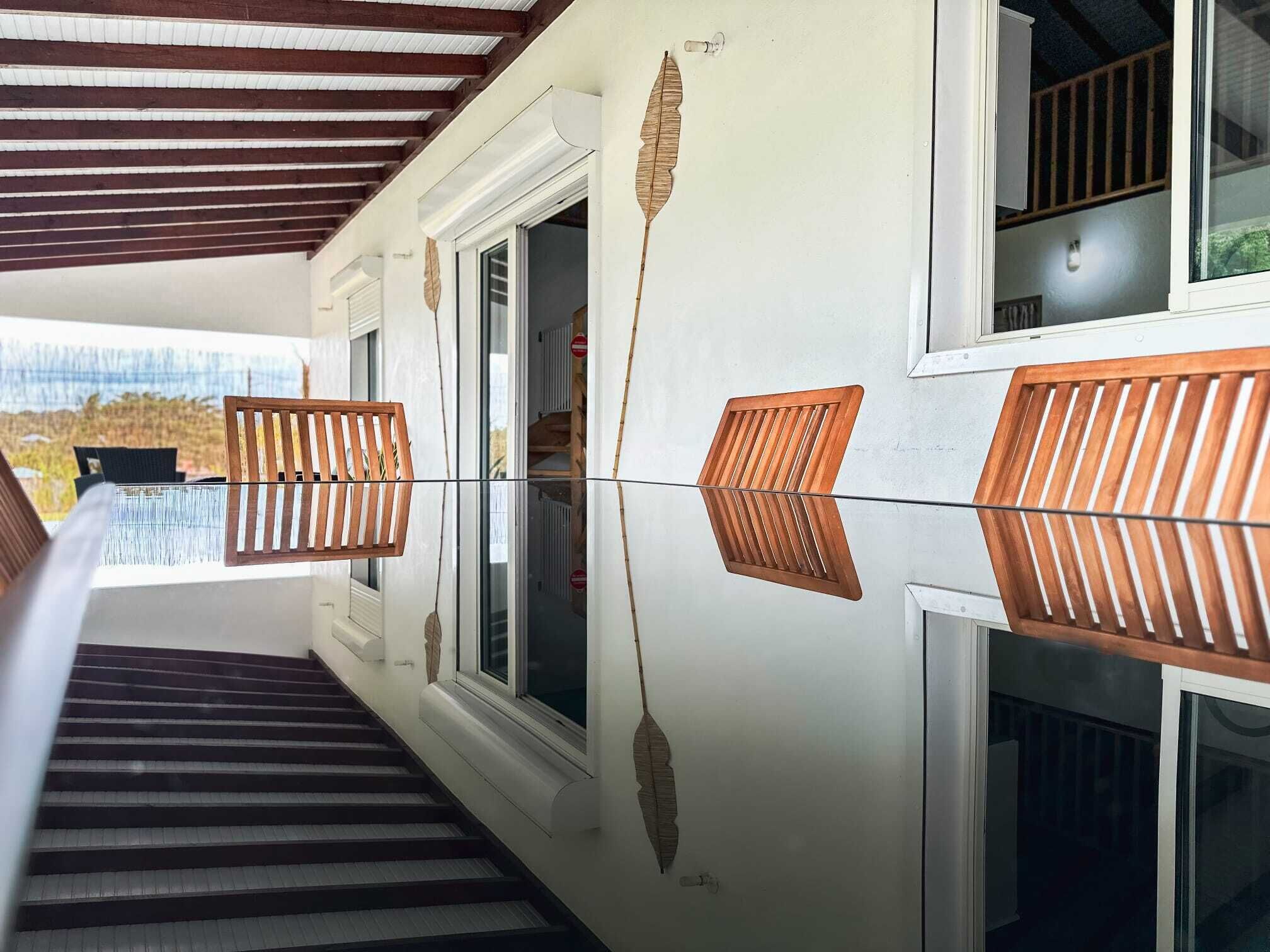 A hallway with a reflective floor, wooden slatted chairs, and a view of the outdoors through a window.