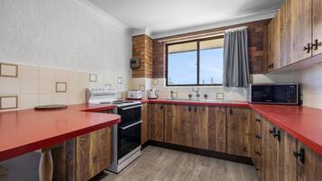 A kitchen with wooden cabinets, a red countertop, a built-in oven, and a window with a curtain.