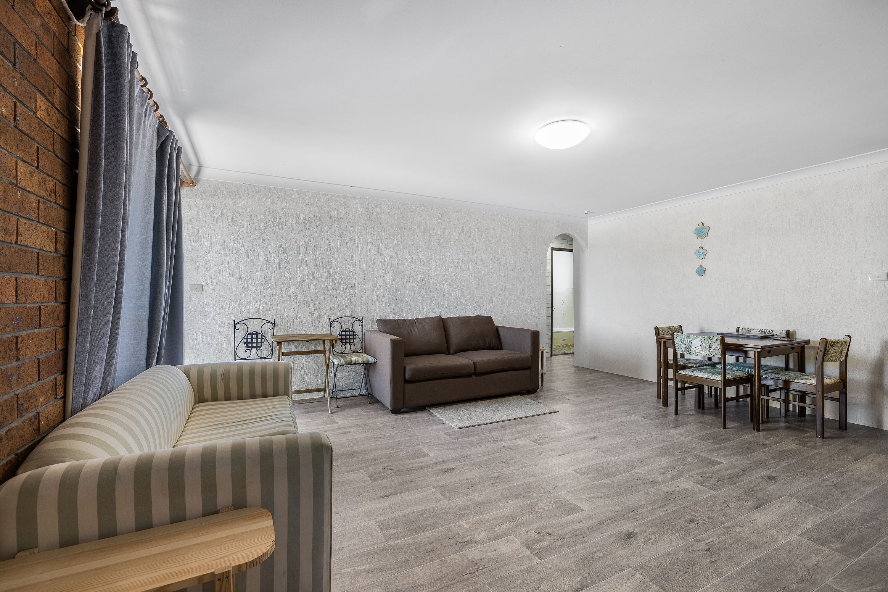 A living room with a sofa, a dining table with chairs, and a brick wall.