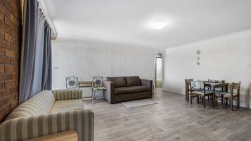 A living room with a sofa, a dining table with chairs, and a brick wall.