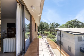 A balcony with a view of a garden and trees, a sliding glass door, and a small seating area with a cushion. - 3 Turtles Unit 6/49 Landsborough St SWR (South West Rocks)