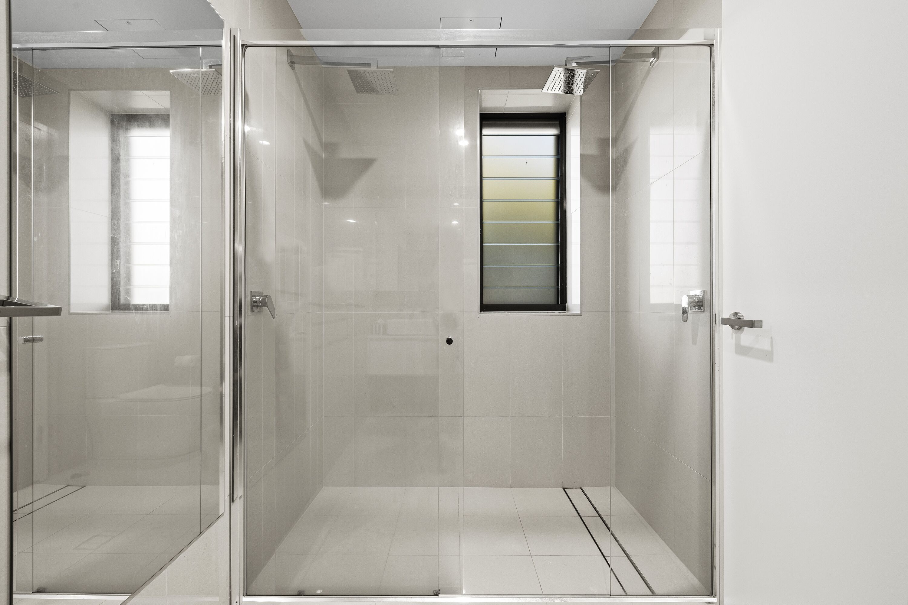 A modern bathroom with a glass-enclosed shower, a small window, and a tiled floor.