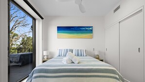 A modern bedroom with a large bed, a view of the outdoors, and a beach painting on the wall. - Paradise on Gregory G04/21 Gregory St SWR (South West Rocks)
