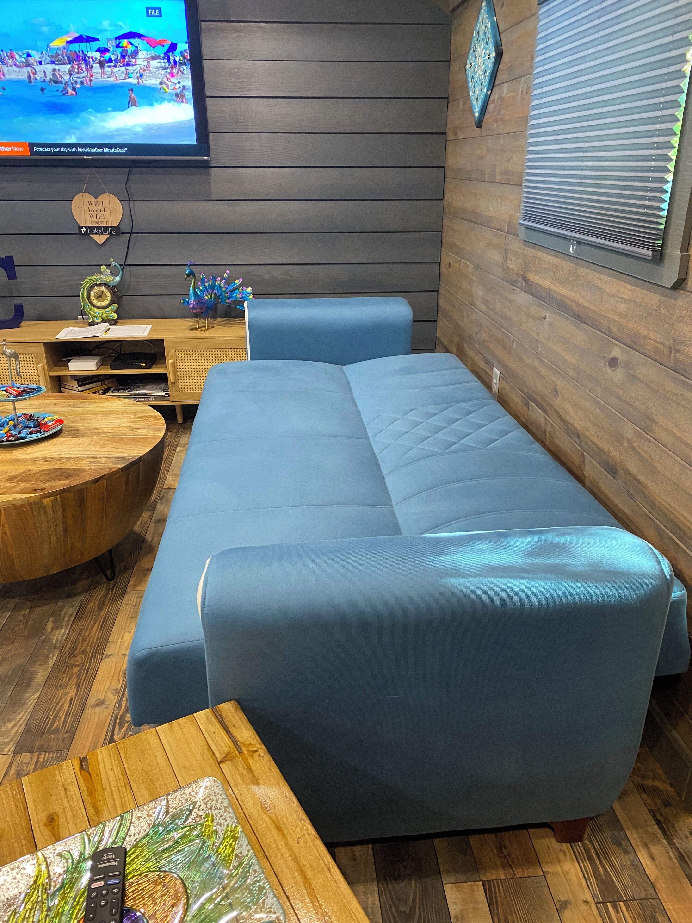 A modern living room with a blue sofa, wooden coffee table, and a TV displaying a beach scene.