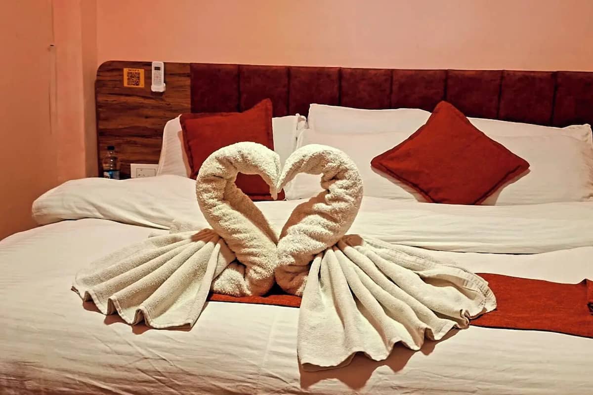 A hotel room with a bed featuring a heart-shaped towel arrangement and red pillows.