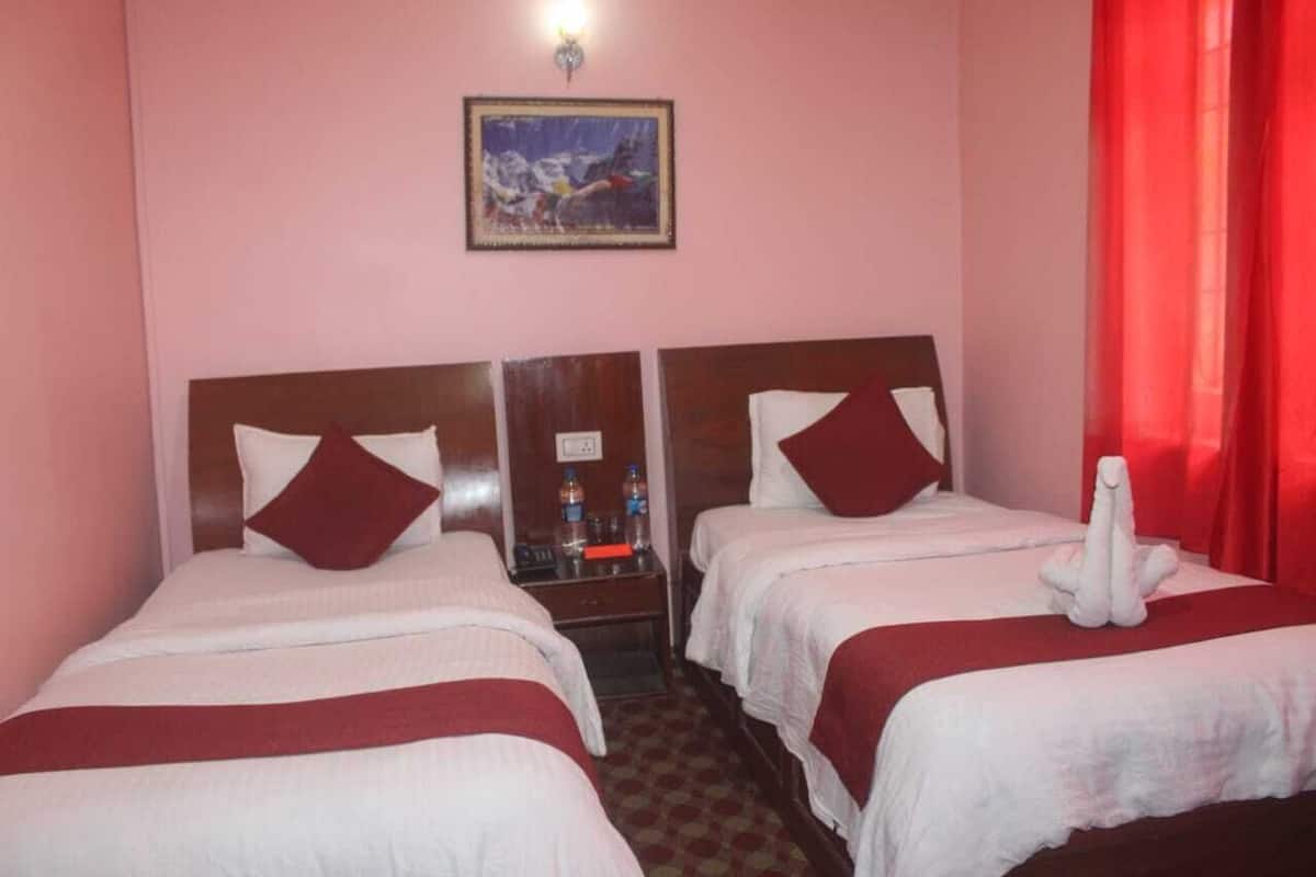 A hotel room with two beds, each with a wooden headboard and white bedding. There is a small table between the beds with a water bottle and a glass. A painting hangs on the wall above the beds.
