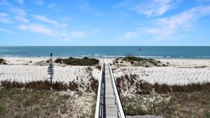 Une promenade en bois menant à une plage bordée de dunes, sous un ciel dégagé.